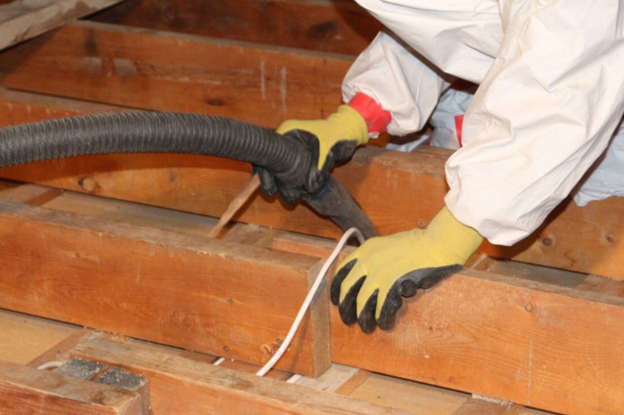 A man wearing a white protective suit works on a wooden floor in an attic, focusing on mold removal in Seattle, WA.